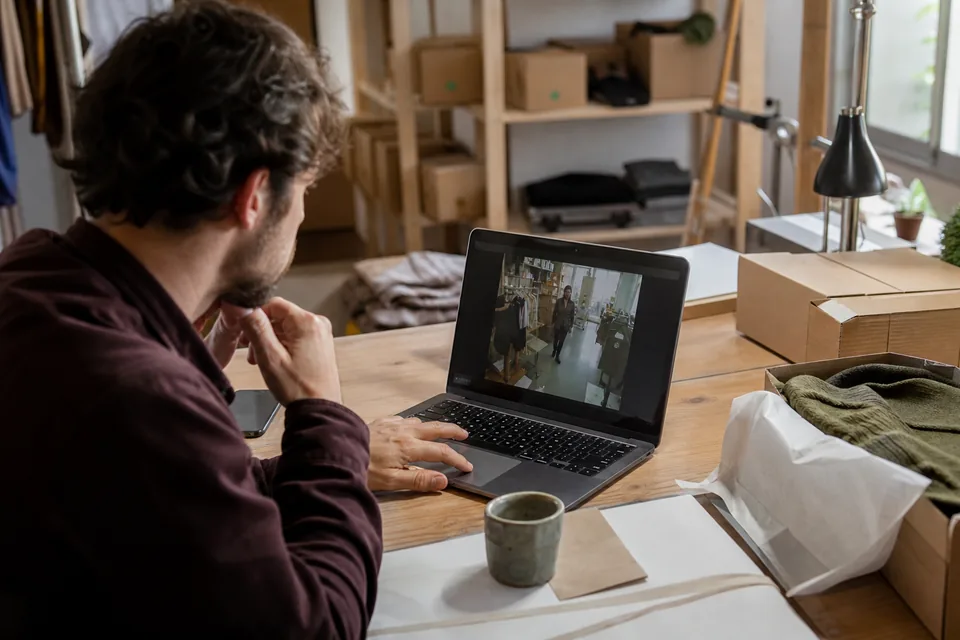 Online store owner reviewing a recorded shopper visit on a laptop beside shipping boxes